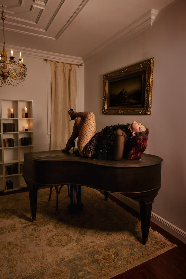 Editorial luxury loungewear campaign shot on a matte black grand piano under a crystal chandelier at a West Palm Beach estate.